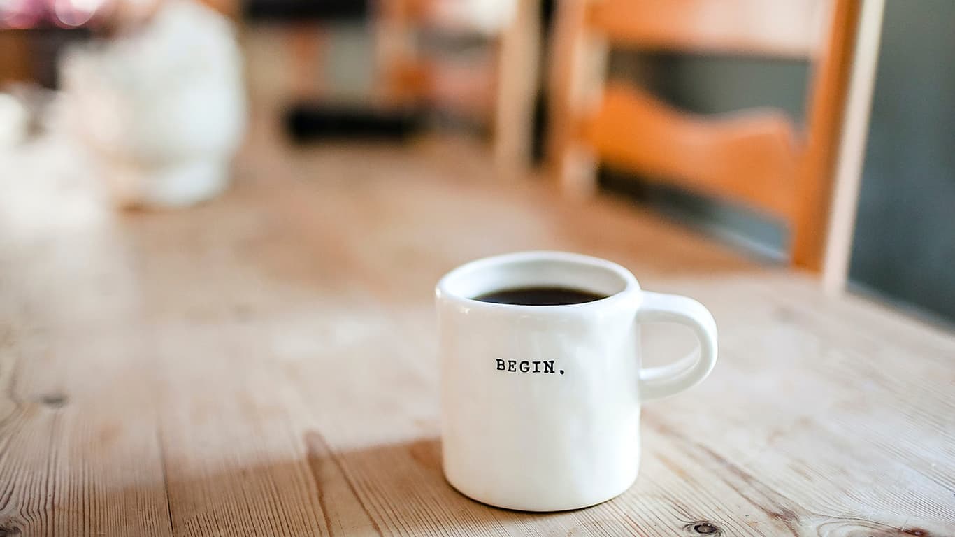 Caneca com café e a palavra "begin", ou "comece", em português, para incentivar o autoconhecimento proporcionado pela Janela de Johari.