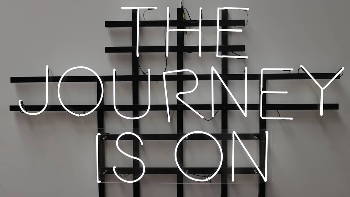 Letreiro luminoso com a frase em inglês "the journey is on" ou "a jornada começou", em português, inspirando a busca pelo autoconhecimento da Janela de Johari.