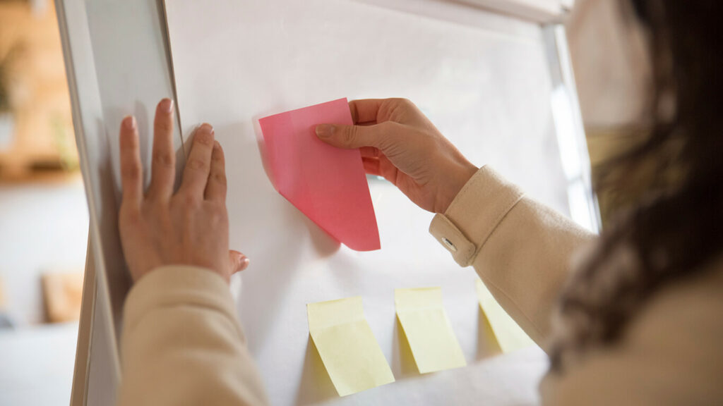 Mulher colocando blocos adesivos em uma lousa e iniciando o método kanban.