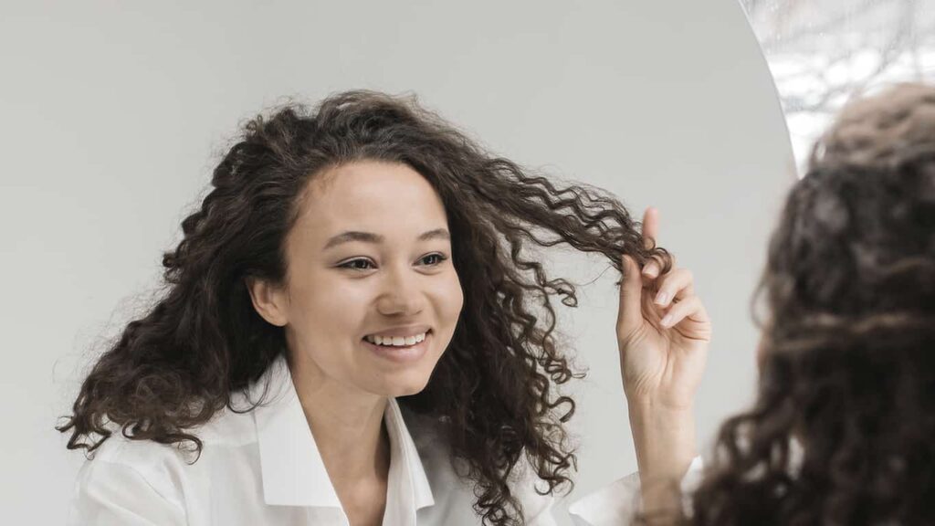 Uma mulher se olha no espelho sorrindo, representando o autocuidado mencionado na palestra sobre saúde mental de Mari Luz.