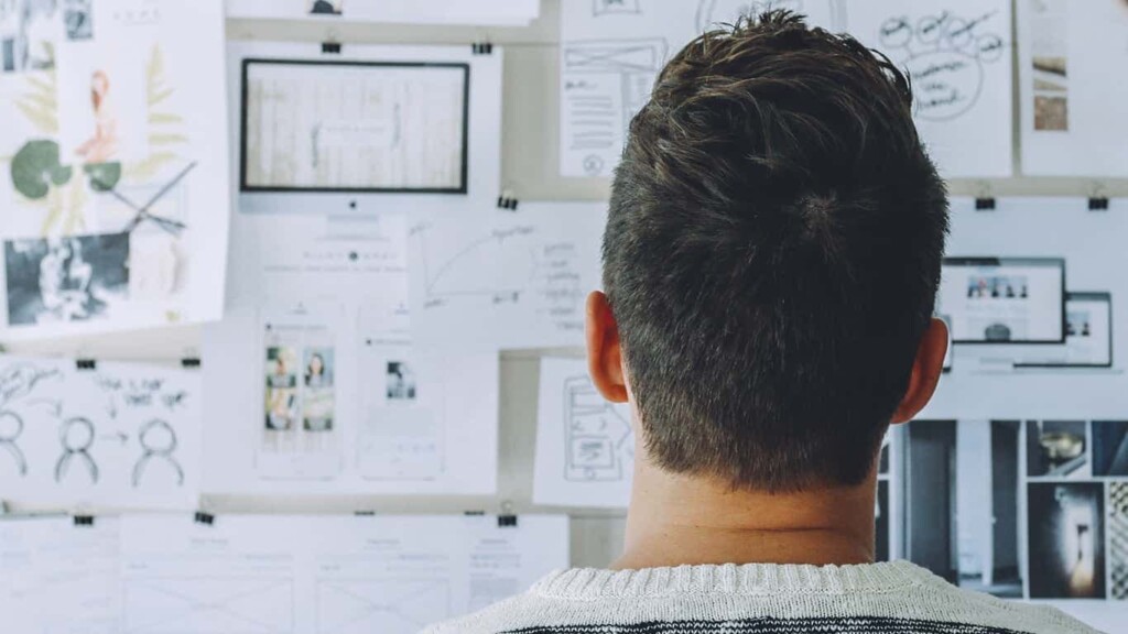 Um homem de cabelo curto está de costas para a câmera e observa um quadro com vários papeis estratégicos, simbolizando a estratégia de mudança do Blog MBA USP/Esalq.