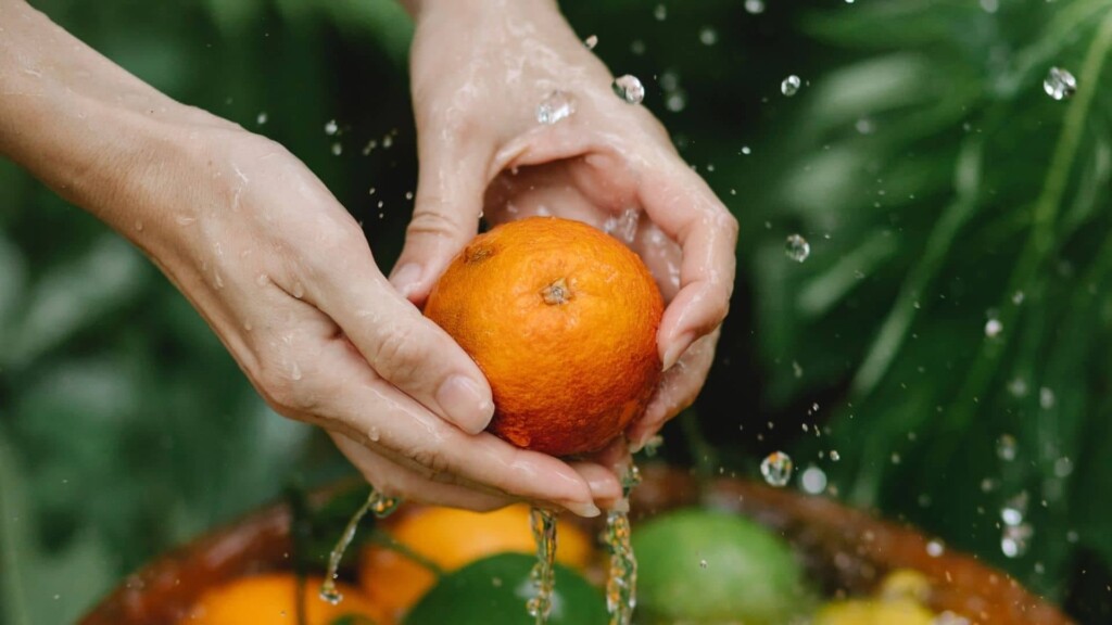 Hand holding a ripe orange in the air on top of a basket with more oranges.