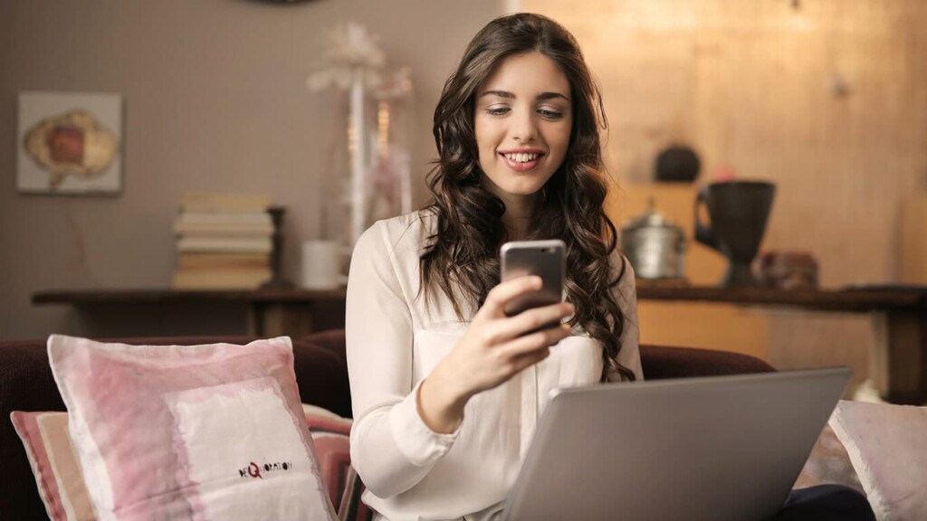 menina sentada com notebook no colo, mexendo no celular e mostrando o uso saudável e consciente do celular