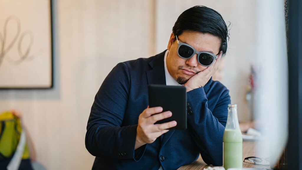Cara de terno e óculos escuros olhando para seu aparelho e não mostrando um uso saudável e consciente do celular.