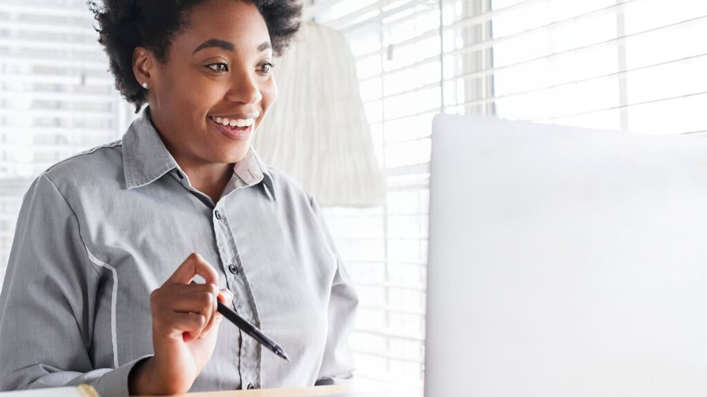 Mulher sentada de frente para o monitor com uma caneta na mão e com cara de surpresa pelos diferenciais oferecidos em sua pós-graduação