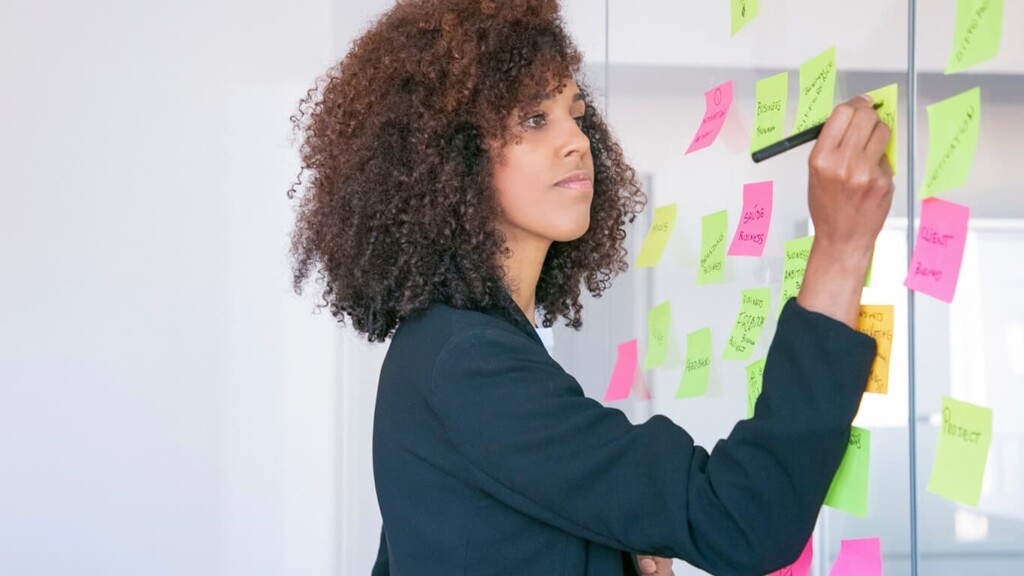 Mulher que escolheu a carreira em Gestão de Projetos escrevendo em uma lousa cheia de post-its