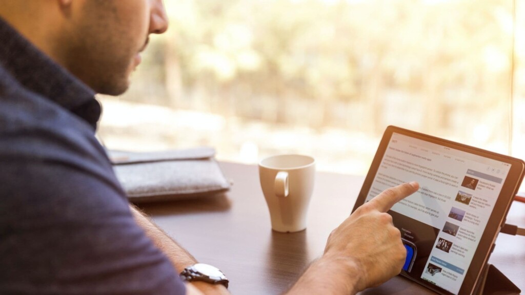 Homem sentado a uma mesa usa um tablet enquanto pensa em como utilizar o LinkedIn para crescer profissionalmente.