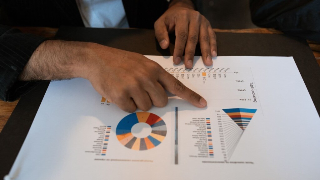 Pessoa fazendo a gestão tributária da empresa senta em uma mesa enquanto aponta para um gráfico impresso em papel.