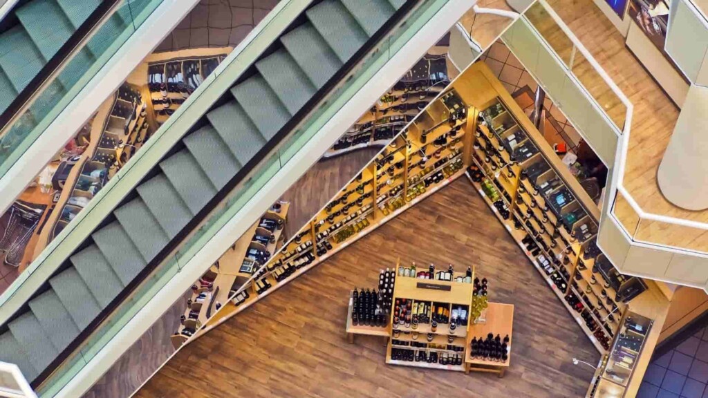 Interior de um prédio de várias andares, com escadas rolantes e várias estantes mostrando diversos produtos.