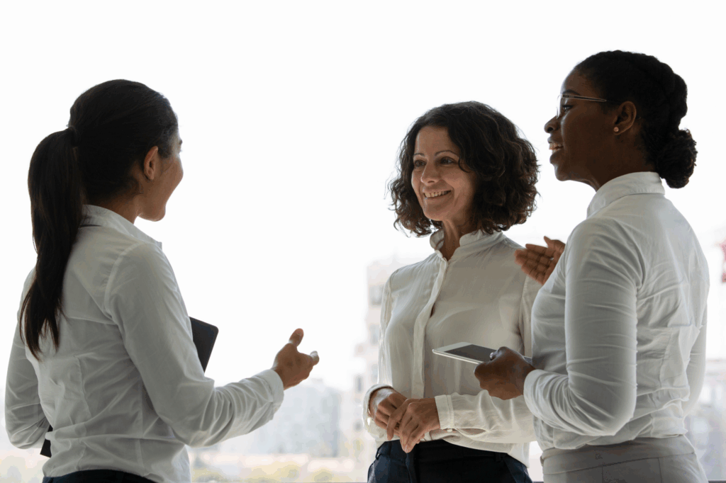 Três mulheres em ambiente corporativo, realizando networking profissional.