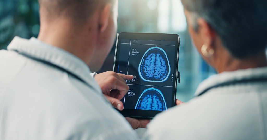 Dois homens de costas utilizando tablet com imagens de cérebros para estudar neurociência.