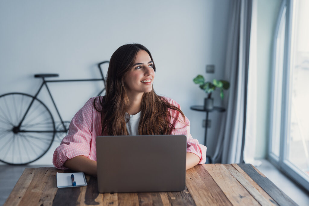 Mulher sorridente olhando pela janela após pesquisar 5 profissões do futuro.