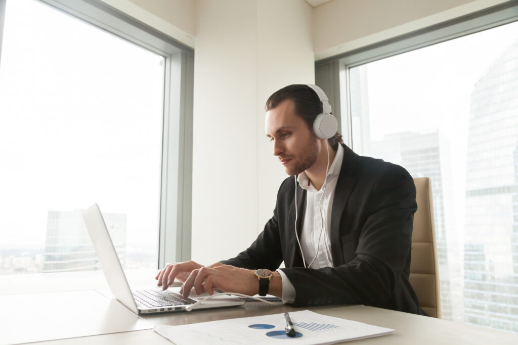 Homem assistindo a uma aula online de MBA em um ambiente corporativo, com fones de ouvido e laptop, ilustrando o aprendizado remoto e a flexibilidade oferecida por programas de MBA.
