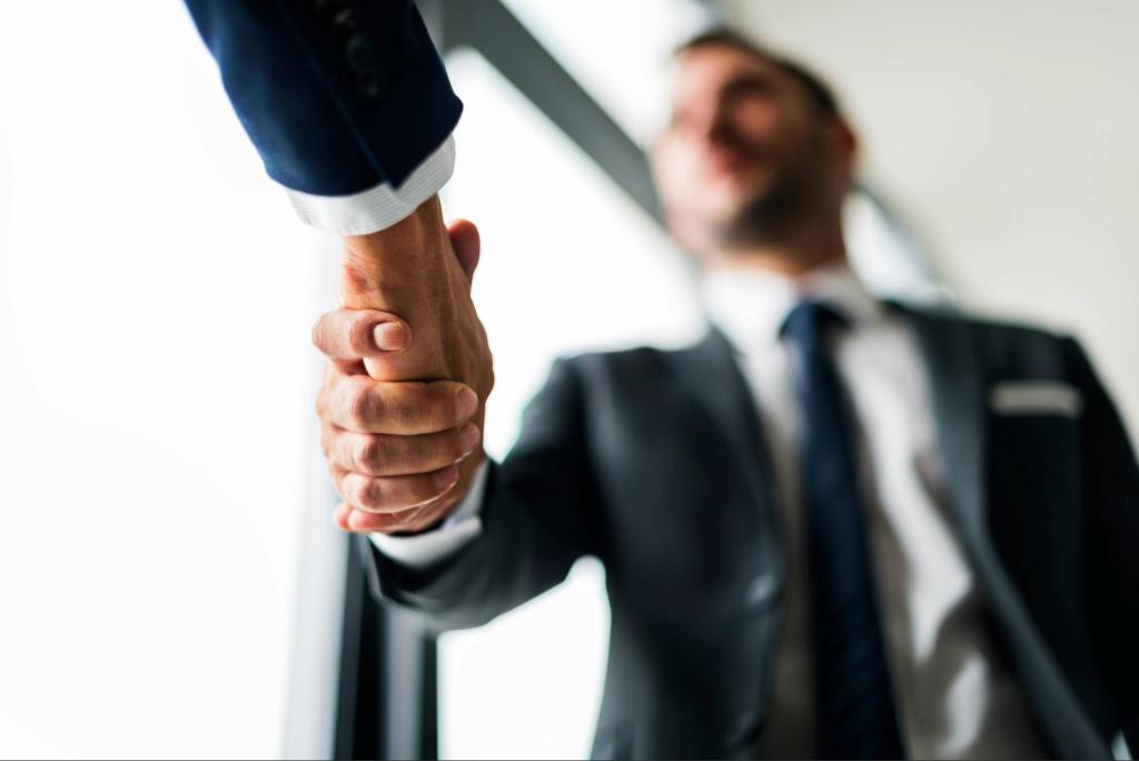 A foto captura dois profissionais em um aperto de mão firme e confiante, simbolizando o fechamento de um acordo ou parceria importante. A imagem transmite um momento de confiança, colaboração e profissionalismo.