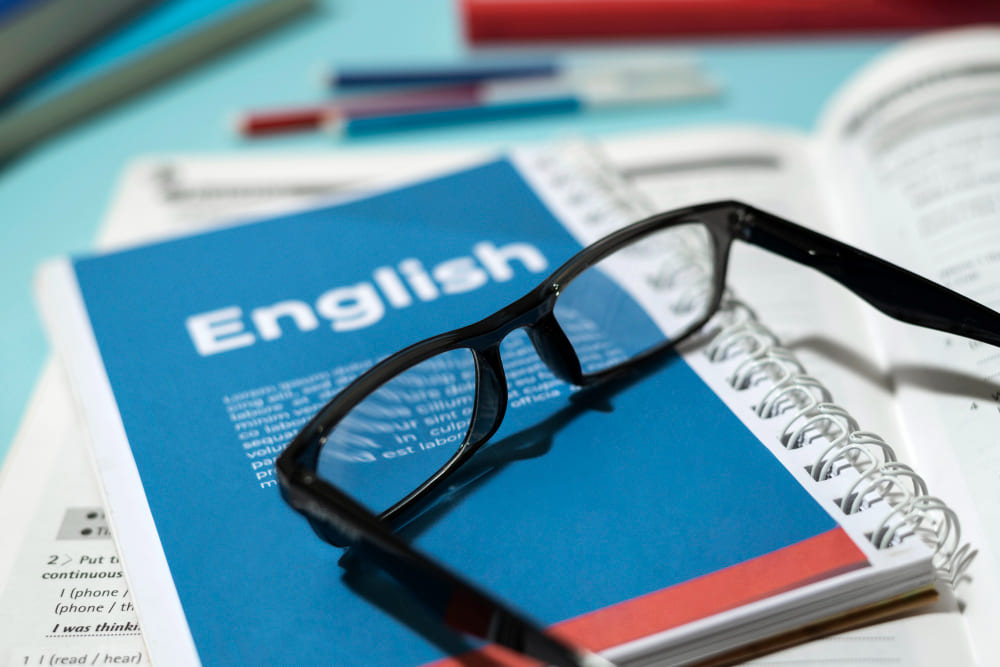 Materiais de estudo de inglês com livro aberto sobre a mesa, representando o aprendizado do idioma como apoio para alavancar a carreira e aproveitar melhor o MBA.