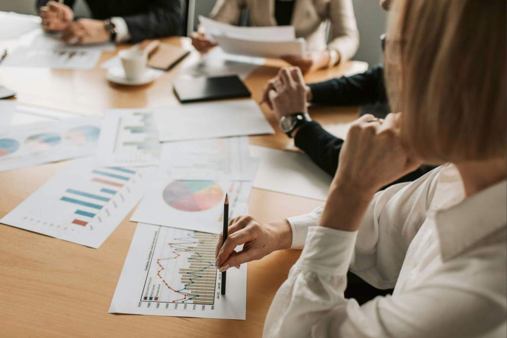 Reunião de negócios focada na análise de dados financeiros. Profissionais observam gráficos de desempenho, indicadores econômicos e tendências de mercado.