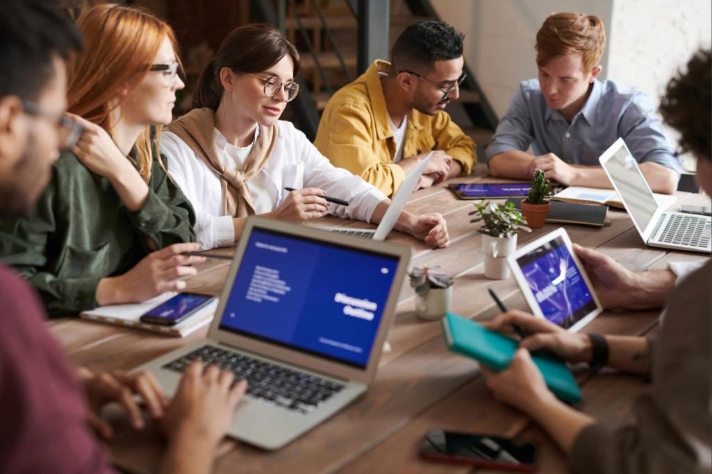 Grupo de profissionais em uma reunião colaborativa, utilizando laptops e tablets para discutir estratégias de transformação digital em um ambiente de trabalho moderno e dinâmico.